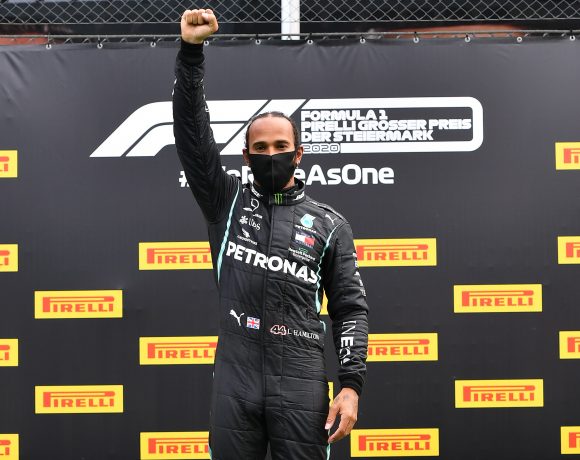 O inglês Lewis Hamilton, vencedor do GP da Estíria no domingo (12), no podium improvisado, faz o seu protesto contra o racismo.